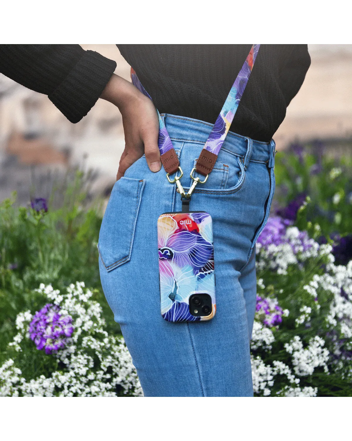 Persoon draagt Samsung A55 5G met vrolijk bloemenhoesje van Mio aan bijpassend koord in een tuinsetting.